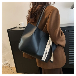 Detail of black matte leather tote with ivory ribbon strap on wool coat background