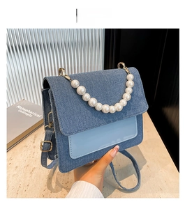 Detailed close-up of blue denim handbag with pearl handle and golden hardware accent