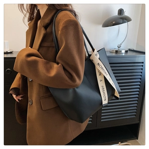 Black large capacity tote bag shown on shoulder over a stylish brown wool coat