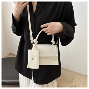Close-up of white minimalist crossbody bag featuring a knotted handle and small pouch
