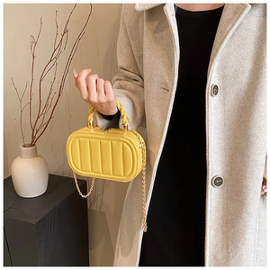 Detail of yellow quilted box bag with spiral handle and gold chain strap on a model