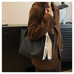 Detail of a black leather tote bag with a branded canvas strap worn over the shoulder