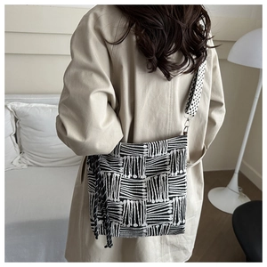 Detail of checkered tote bag with wide strap and tassel knot on a neutral background