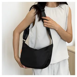 Detail of black nylon crescent crossbody bag with orange tag and wide strap on model