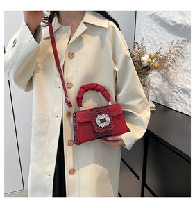 Detail of burgundy croc-embossed handbag with rhinestone buckle on beige coat model