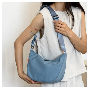Blue canvas dumpling bag detail with adjustable strap and orange side label on model
