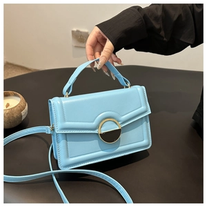 Detail of light blue crossbody bag featuring a round gold metal buckle and leather texture