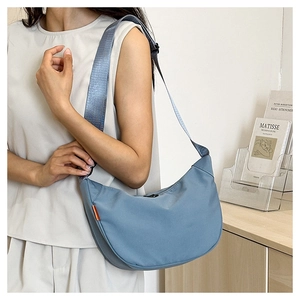 Detail of blue crescent crossbody bag with wide strap and orange label accent