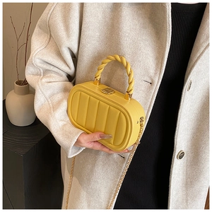 Detail of yellow quilted box bag with woven handle and gold chain strap in hand