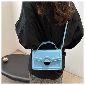 Detail of light blue leather crossbody bag with modern gold and black metal clasp design