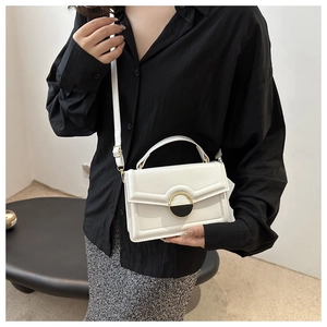 Detailed view of a white leather crossbody bag featuring a golden circular clasp and a slim strap