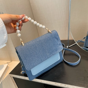 Contrast denim handbag with pearl handle and shoulder strap shown in mirror reflection