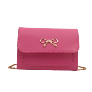 Petit sac carré rose avec nœud doré et bandoulière en chaîne dorée sur fond blanc