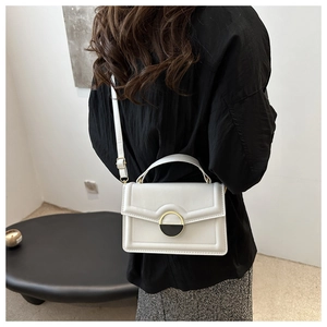 Detail of white leather crossbody bag featuring unique gold and black metal buckle