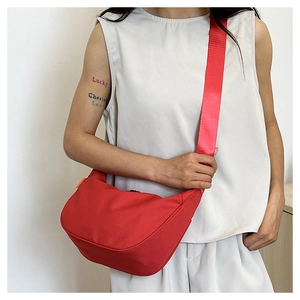 Detail of red crescent dumpling bag with wide adjustable shoulder strap worn by a model