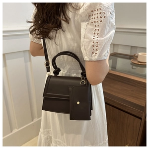Detail of dark brown leather crossbody bag with knot handle and mini charm pouch accessory
