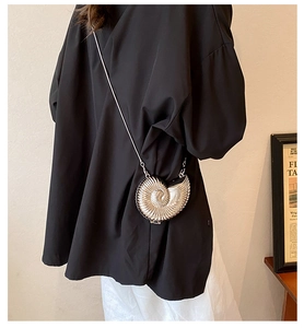 Artistic silver conch-shaped metal crossbody bag with chain strap shown on model