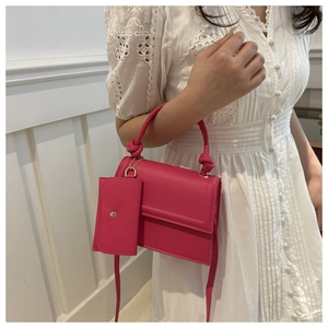 Detail of rose red crossbody bag with mini pouch and knotted handle on lace dress