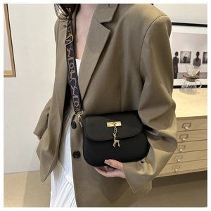 Detail of black crossbody bag with gold deer charm and patterned wide strap