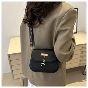 Détail du sac coquille noir mat avec pendentif girafe dorée et bandoulière imprimée