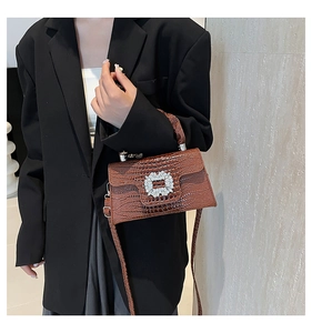 Detail of crocodile pattern handbag with crystal buckle and long shoulder strap