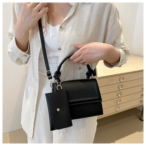 Detail of a matte black square crossbody bag with chain accessory on a neutral background