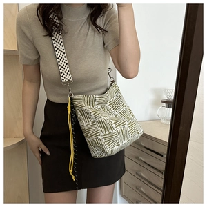 Detail of canvas tote bag with green geometric patterns and checkered woven shoulder strap