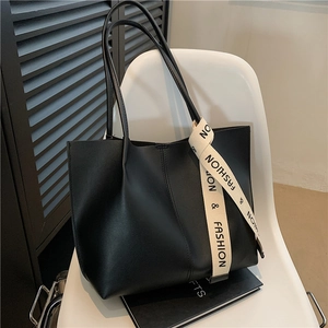 Grand sac cabas noir tendance avec sangle à ruban lettré posé sur une chaise blanche