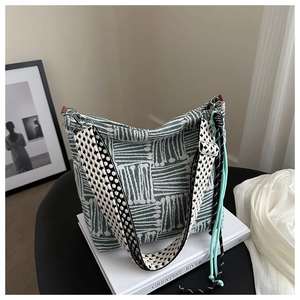 Detail of green and white woven hobo bag with wide strap on a white book