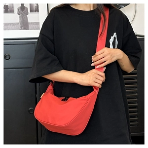 Detail view of a red waterproof nylon moon bag with wide shoulder strap worn by a model