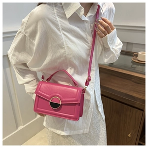 Detail view of pink crossbody bag with a distinctive round gold and black metal buckle