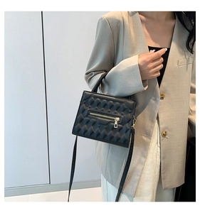 Detail view of black quilted leather bag with gold zipper held by model in gray suit