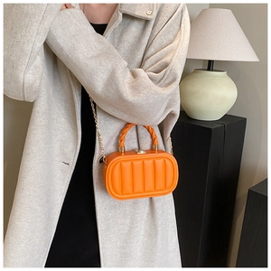Detailed view of orange quilted mini box bag with woven handle and gold chain strap