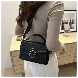 Detail view of a black leather square handbag with a prominent round gold metal lock