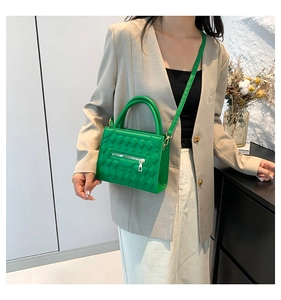 Close-up of bright green quilted leather crossbody bag with zipper detail on beige suit