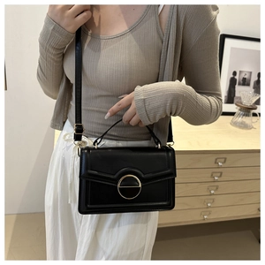 Close-up of black minimalist crossbody bag featuring a round gold metal buckle and hand strap