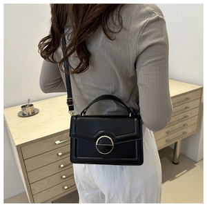 Detail of a black leather crossbody bag with a round gold buckle and a top handle