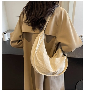 Détail du sac dumpling blanc cassé avec tissu texturé porté sur un trench-coat kaki