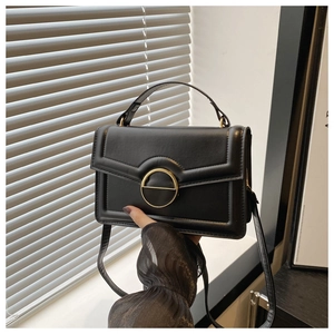 Detail of a black leather crossbody bag with quilted edges and a gold circular buckle