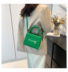 Detail of emerald green quilted crossbody bag with top handle and textured faux leather finish