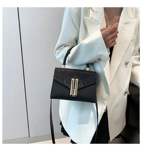 Detail of elegant black shoulder bag with shimmering flap and gold H metal buckle