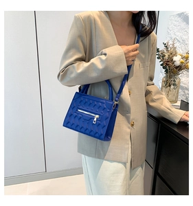 Detail of bright blue crossbody bag with geometric quilted pattern and metallic zipper