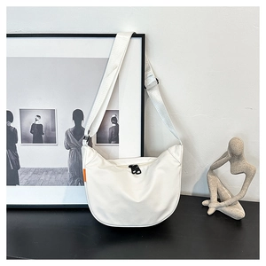 Detail of off-white crescent crossbody bag featuring black zippers and orange side label