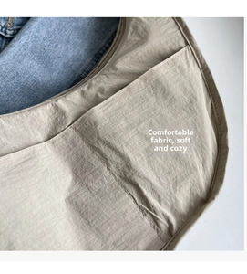 Détail de la sacoche beige montrant les coutures précises et la poche latérale pratique