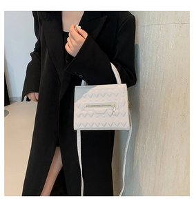 Detail of white quilted crossbody bag with golden zipper and V-shaped stitching texture
