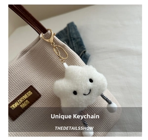 White plush cloud charm with smiley face detail attached to a corduroy tote bag