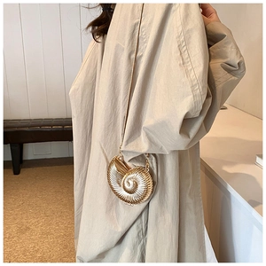Detail of shell-shaped gold crossbody bag with spiral texture and sleek chain strap
