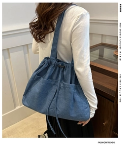 Detail of blue denim tote bag with drawstring closure and front pockets on model