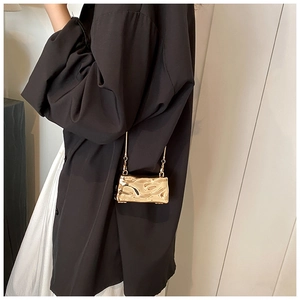 Close-up of golden mini chain bag featuring unique metallic pleated texture on model