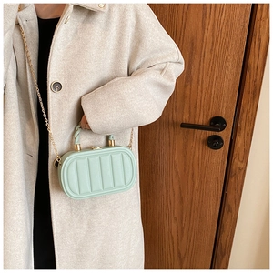 Detail of mint green quilted oval handbag with gold chain strap on cream wool coat